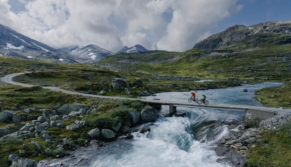 Ungt par på sykkeltur i Koldedalen sykler over bro med storslått bakgtunn