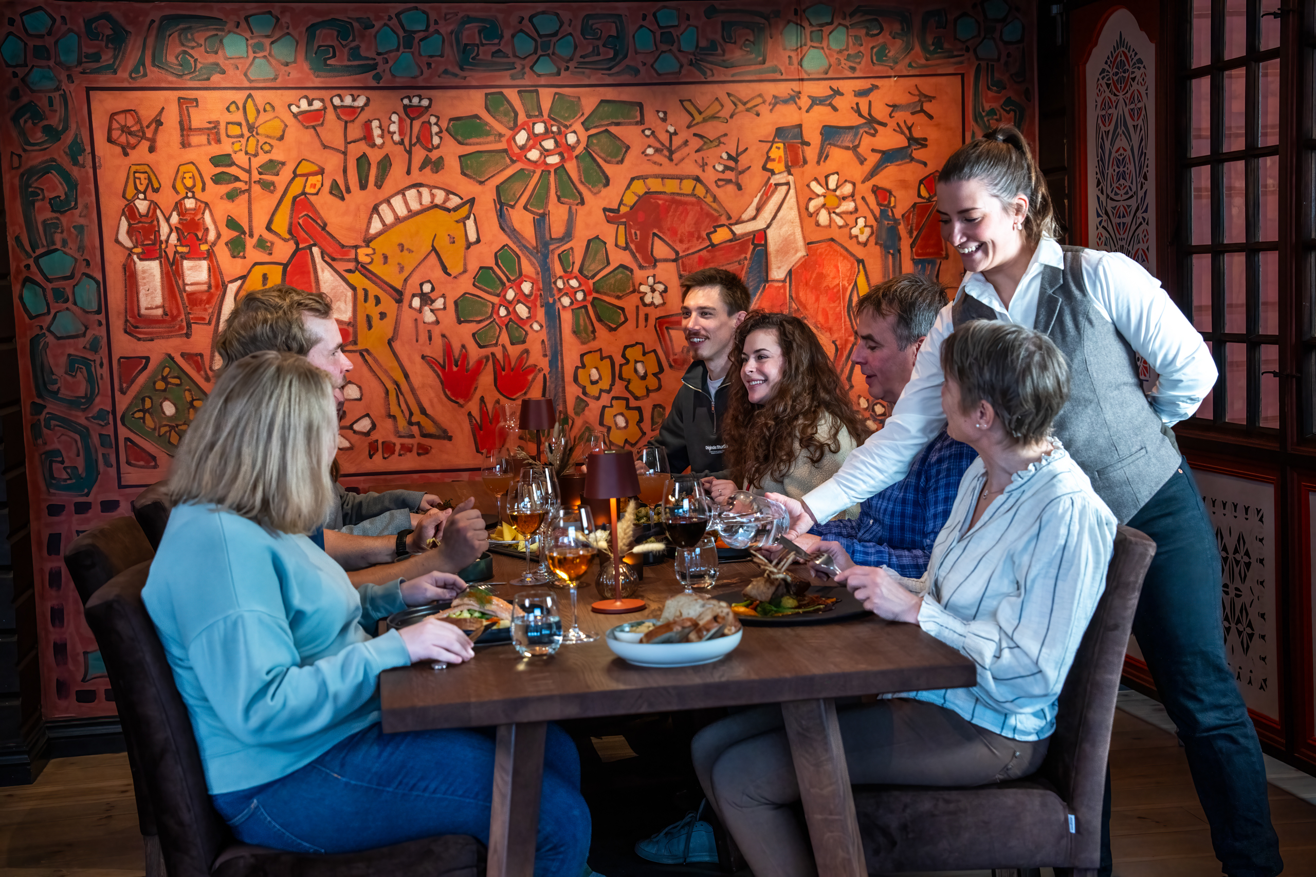 Servitør som serverer en gruppe med venner og familier som nyter et måltid sammen på Filefjellstuene, 