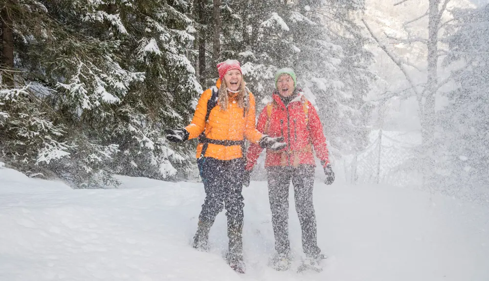 To kvinner på truger som smiler og ler og kaster snø i luften