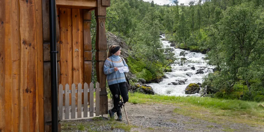 Ung kvinne med fiskeutstyr ser på elven ved siden av en av leilighetene på Filefjellstuene