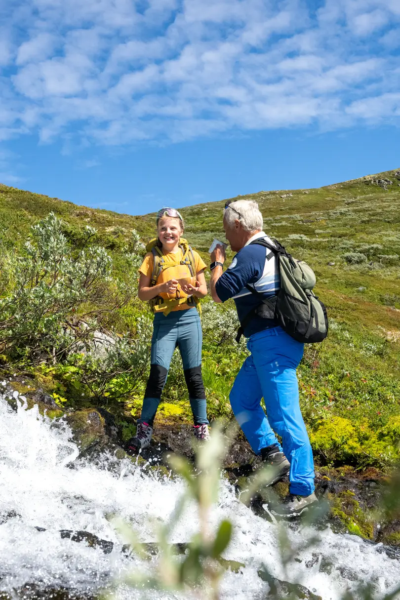 Grandfather and children take a break to drink mountain water from the stream during a mountain hike